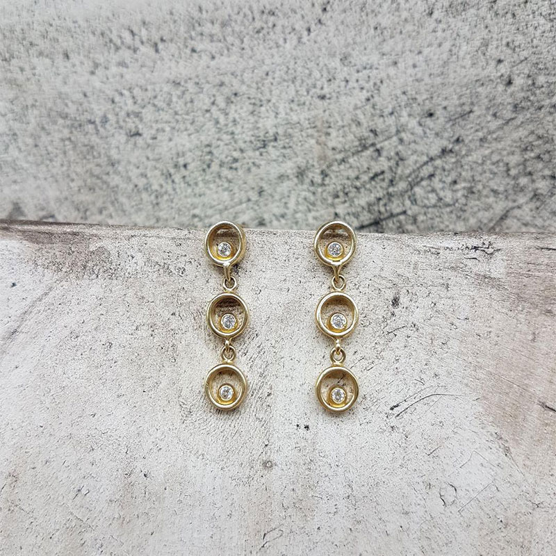 Γυναικεία χρυσά σκουλαρίκια Κ14 αποτελείται από 3 κύκλους διακοσμημένη με λευκά ζιργκόν. 